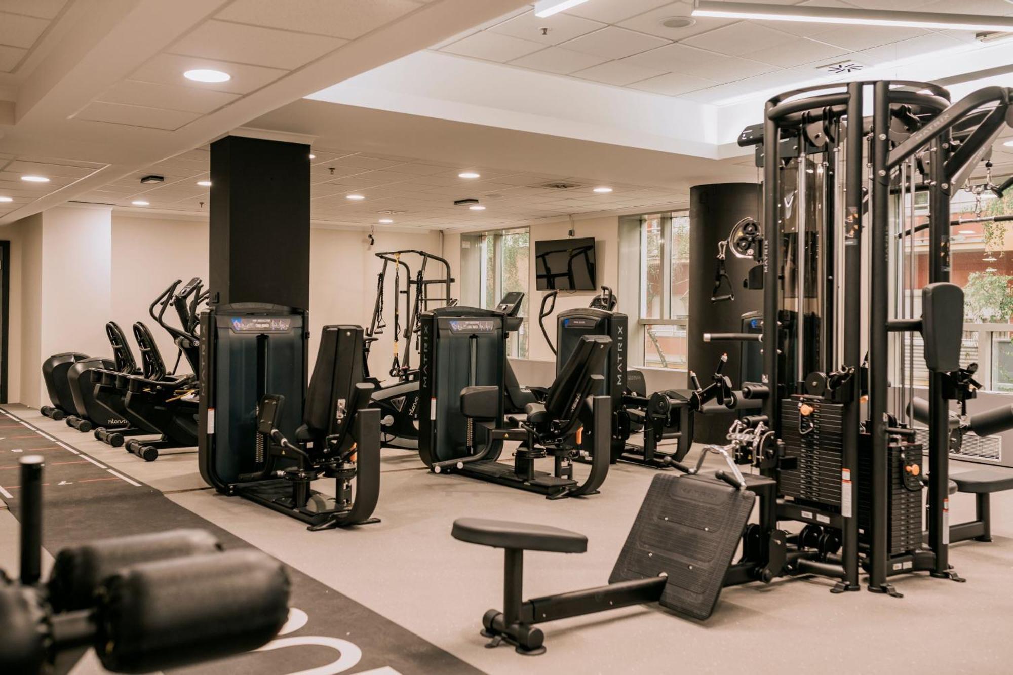 Sheraton Zagreb Hotel Luaran gambar The photo shows a modern gym interior equipped with various exercise machines. There are several cardio machines, such as stationary bikes, along one side. In the center, there is a multi-station weight training machine. The floor is covered with a s